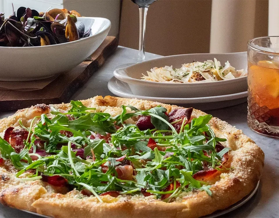 Restaurant table with pizza, mussels, a cheesy dish, and drinks.