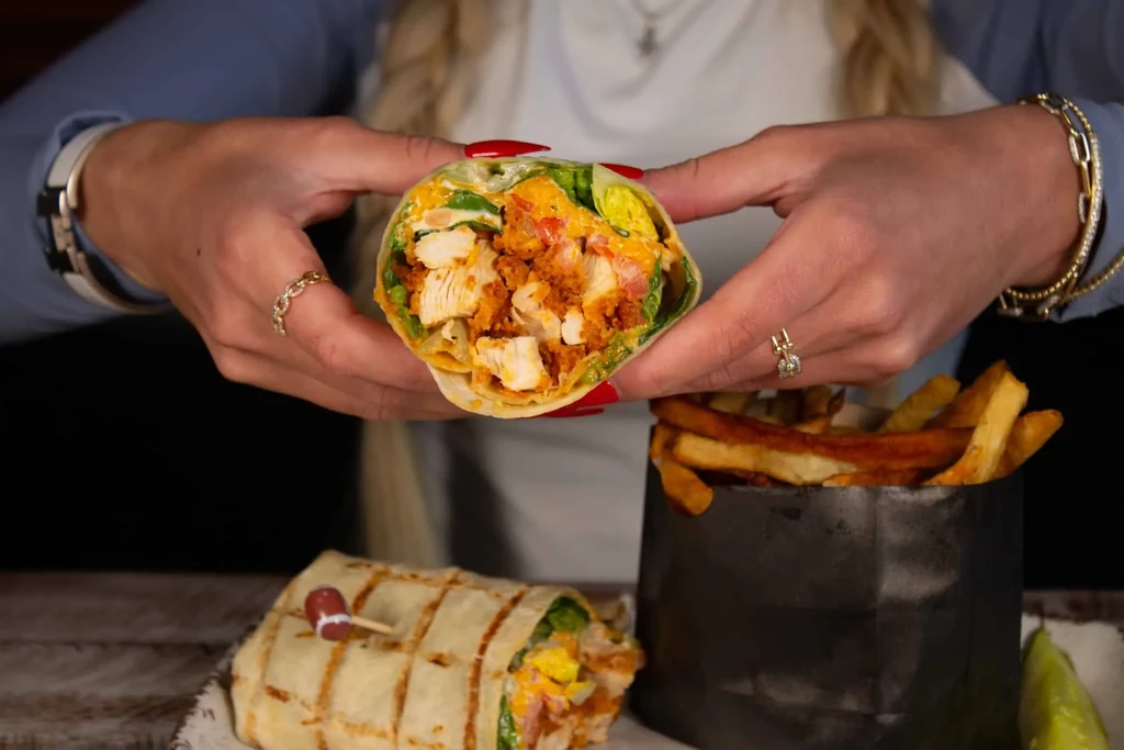 Hands holding an open chicken wrap, with fries and another.