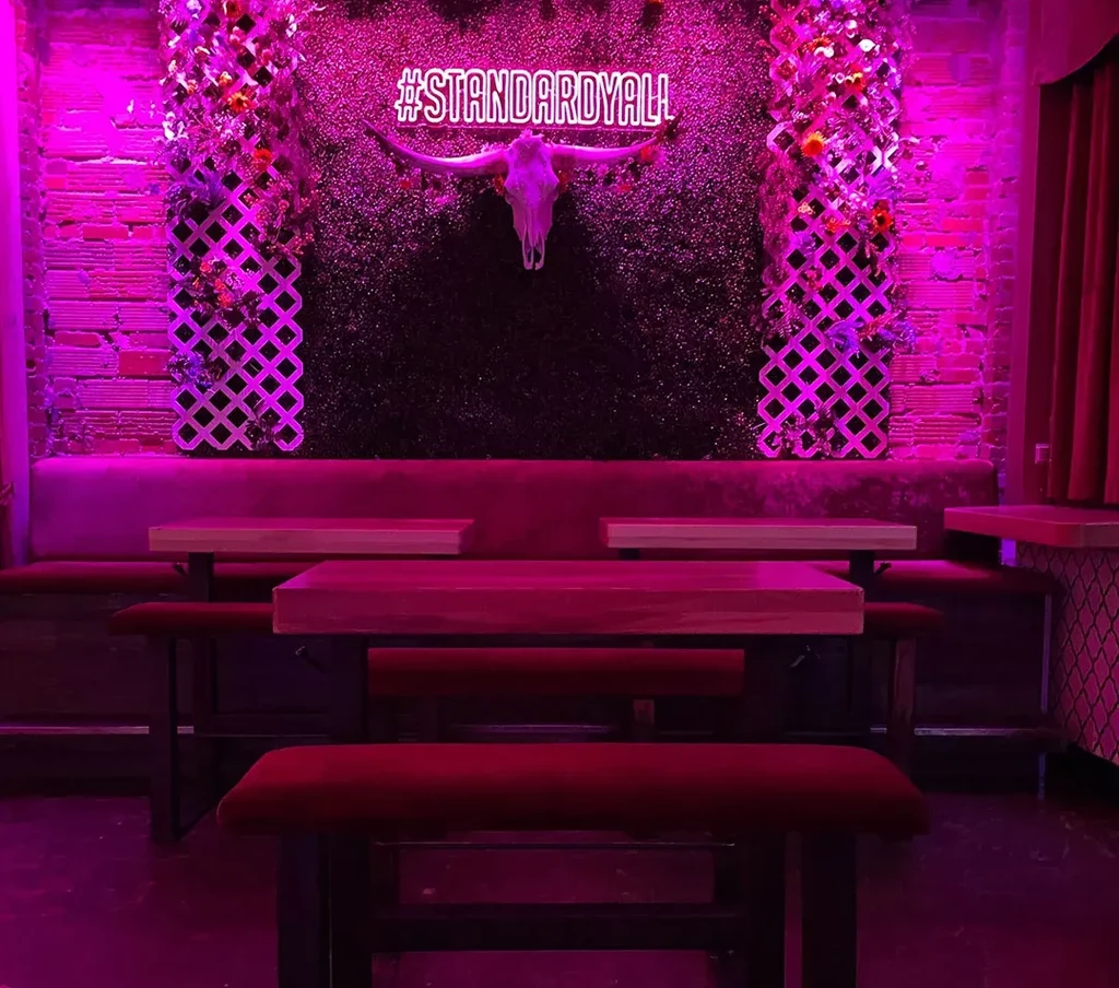Magenta-lit modern bar with velvet banquette, animal skull, and neon sign.