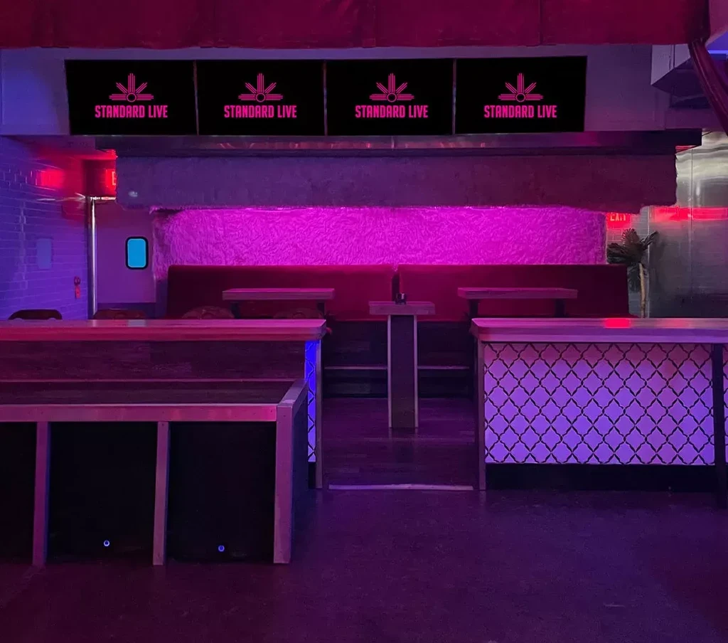 Pink and purple lit bar interior with 'STANDARD LIVE' screens.