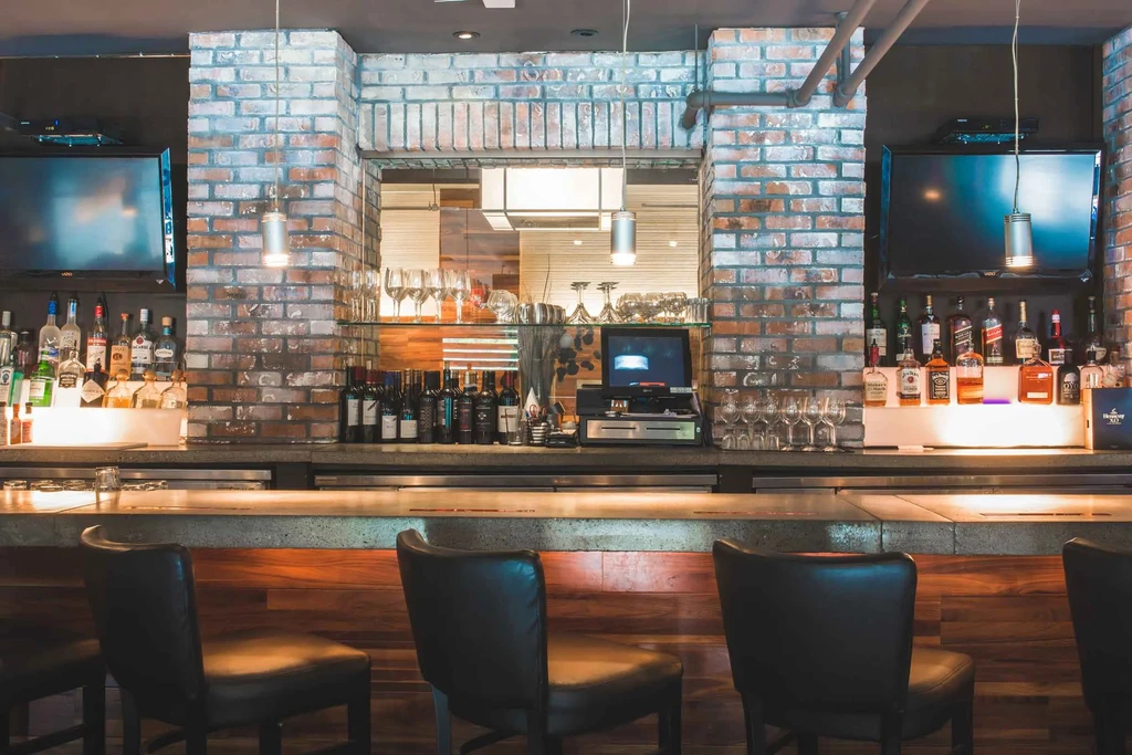 Restaurant bar with concrete counter, brick wall, and backlit liquor shelves.