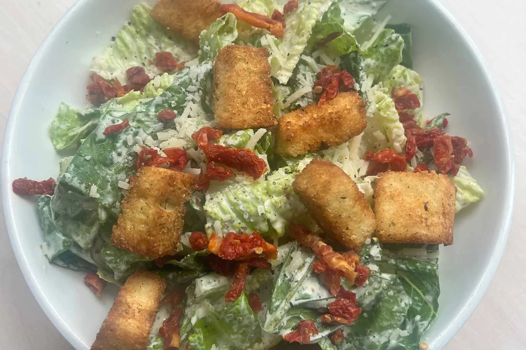 Top-down Caesar salad with lettuce, dressing, cheese, croutons, sun-dried tomatoes.