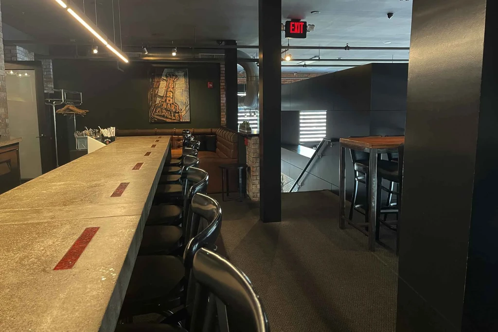 Modern bar interior with long concrete counter, red accents, and dark seating.