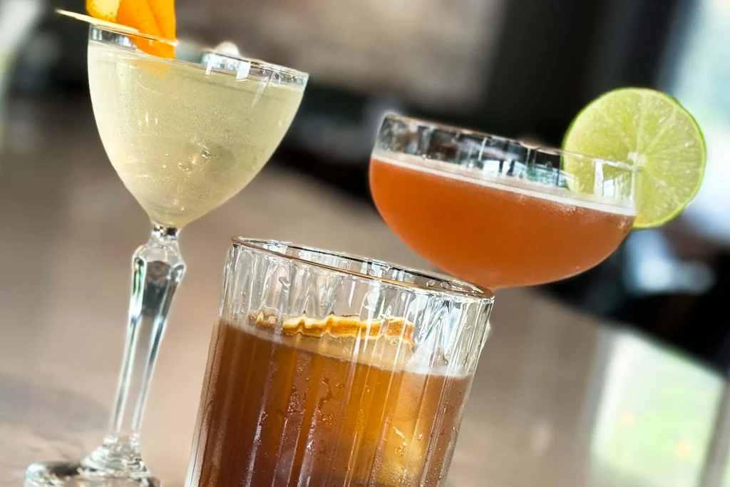 Three distinct cocktails with different garnishes on a polished bar.