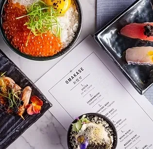 Overhead view of an Omakase menu and several high-end Japanese dishes.
