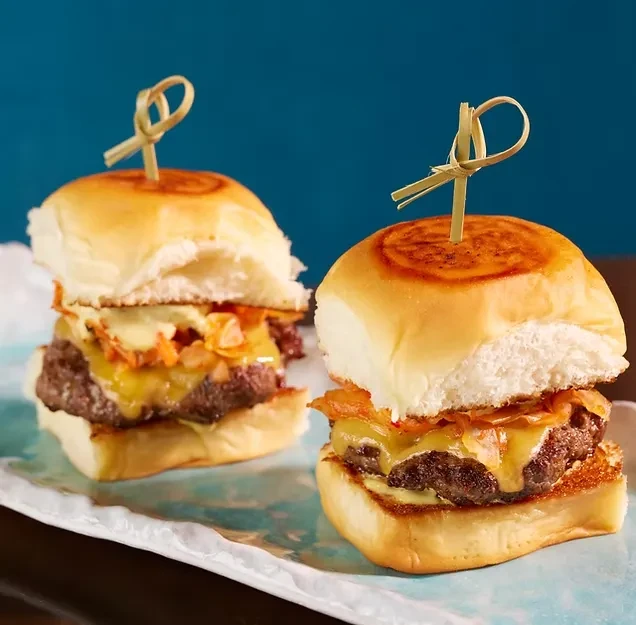 Two sliders with melted yellow cheese and bamboo skewers.