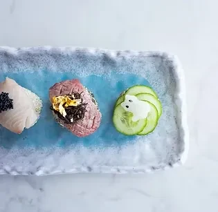 Three small sushi-style dishes on a blue, textured rectangular plate.
