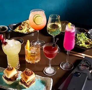 Colorful cocktails, food, a smartphone, and glasses on a dark table.
