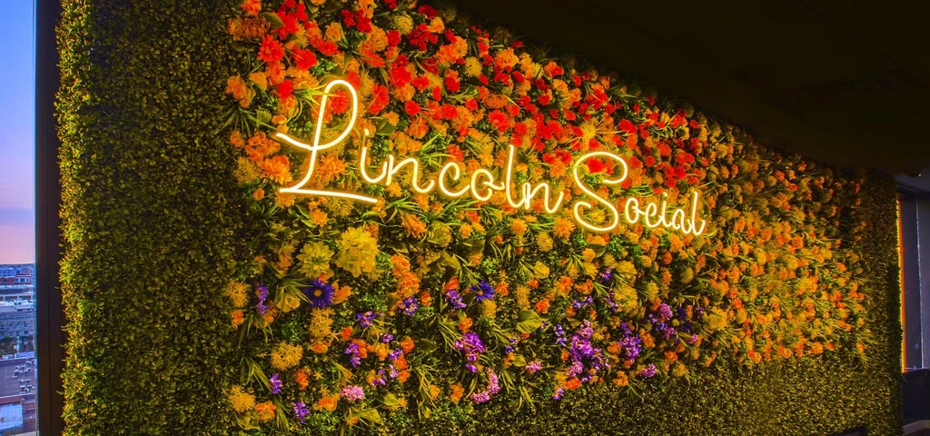 Lush green wall with colorful flowers and 'Lincoln Social' neon sign.