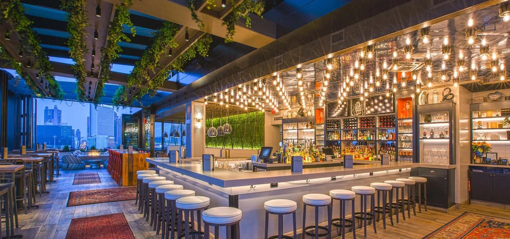 Extensive modern rooftop bar interior overlooks an illuminated city skyline.