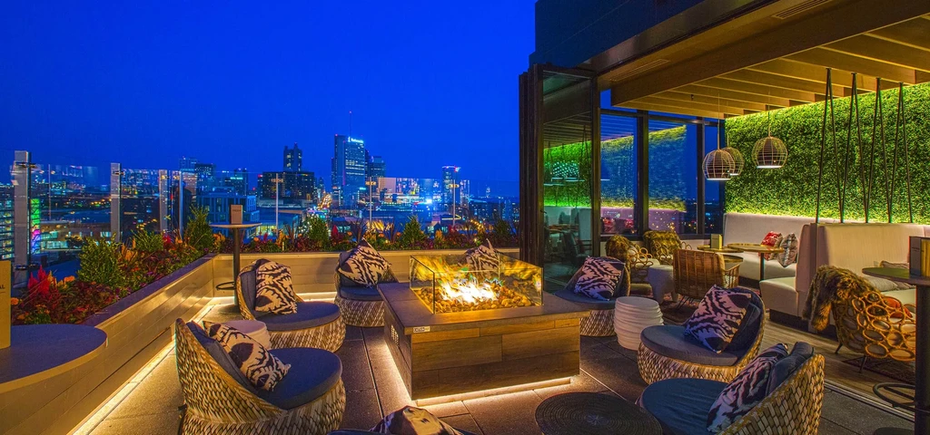 Luxurious rooftop restaurant at night with city skyline and fire pit.