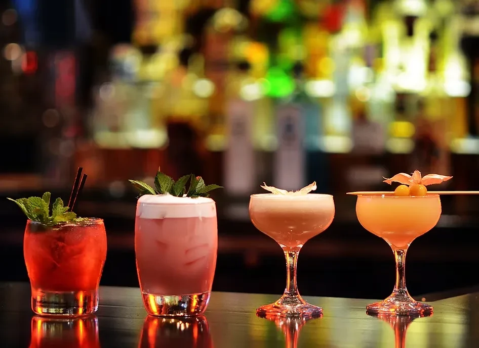 Four intricately garnished cocktails on a dark, reflective bar counter.