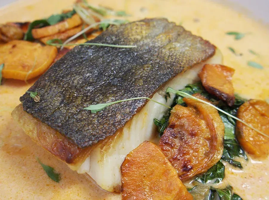 Crispy fish, roasted orange vegetables, greens, creamy sauce, garnished with herbs.