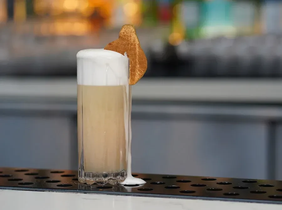 Textured glass with creamy drink, frothy overflowing foam, and fruit crisp.