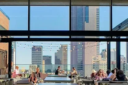 Outdoor rooftop restaurant, string lights, patrons, and panoramic city view.