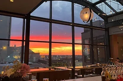 Modern restaurant overlooking a vibrant city sunset through floor-to-ceiling windows.