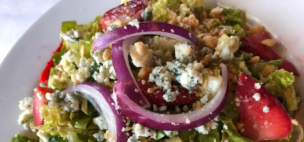 Colorful salad with green lettuce, blue cheese, strawberries, and red onion.