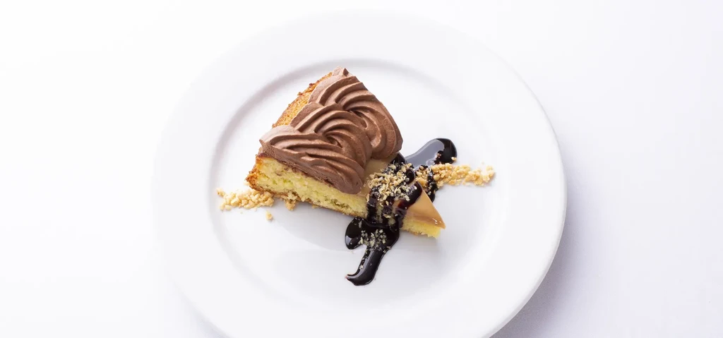 Light cake slice with chocolate cream, caramel piece, chocolate sauce, and nuts.