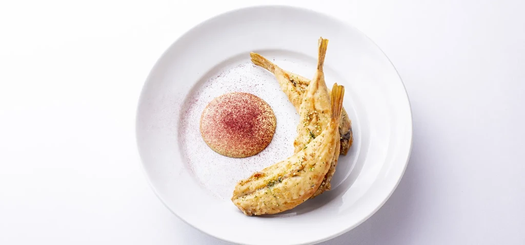Two golden-brown fried fish with sauce and reddish-purple powder on a plate.
