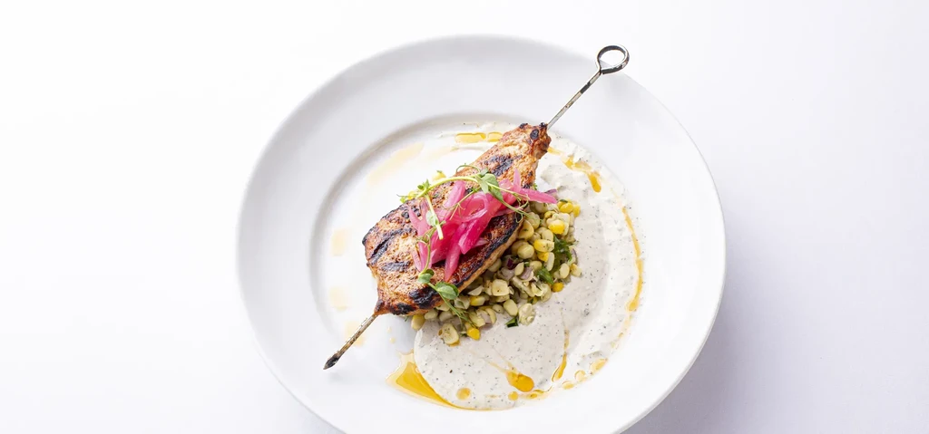 Golden-brown grilled skewer, corn salad, pickled onions, and creamy sauce.
