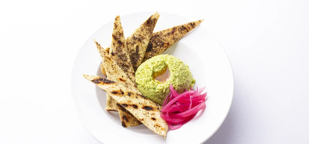 Green dip with oil, grilled pita, and pink pickled onions.