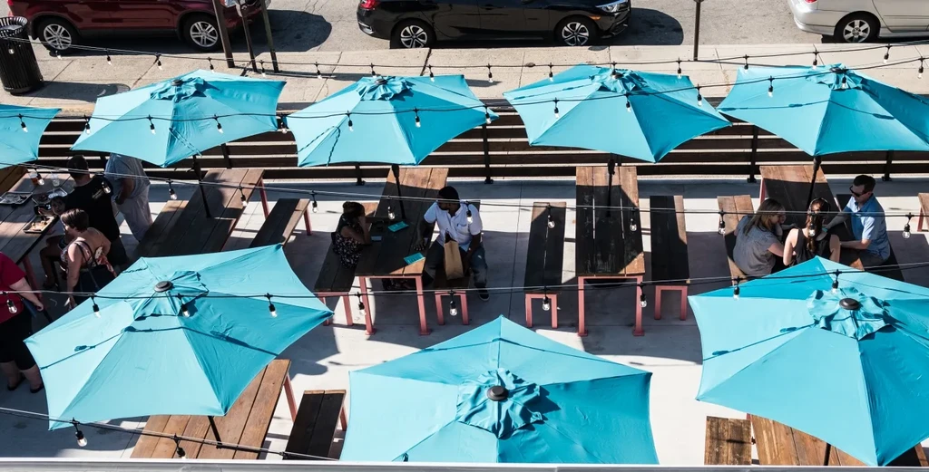 Restaurant patio with turquoise umbrellas, string lights, and people.
