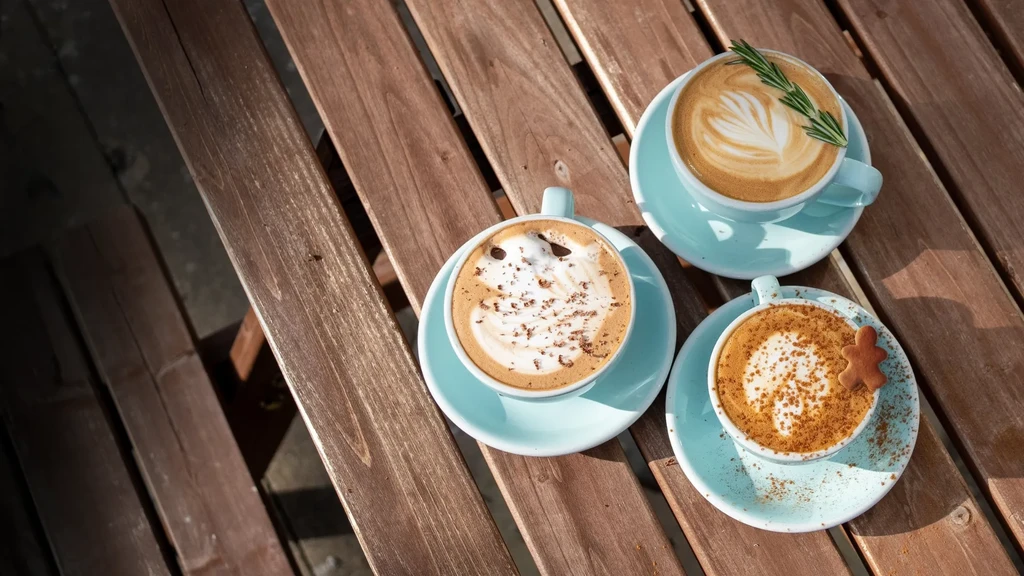 Overhead: three blue coffees with art, spices, gingerbread on wood.