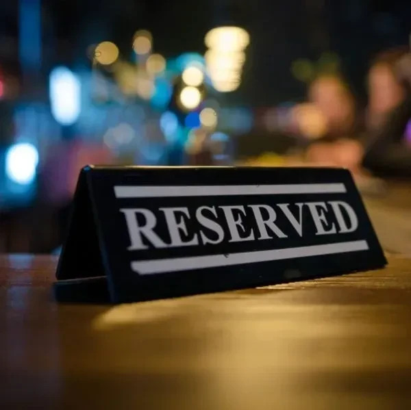 Black triangular 'RESERVED' sign on wooden table, blurred bokeh background.