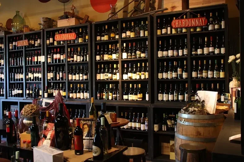 Wine shop shelves densely packed with numerous red and white bottles.