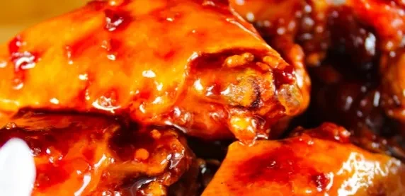 Close-up of chicken wings coated in glossy reddish-orange sauce.