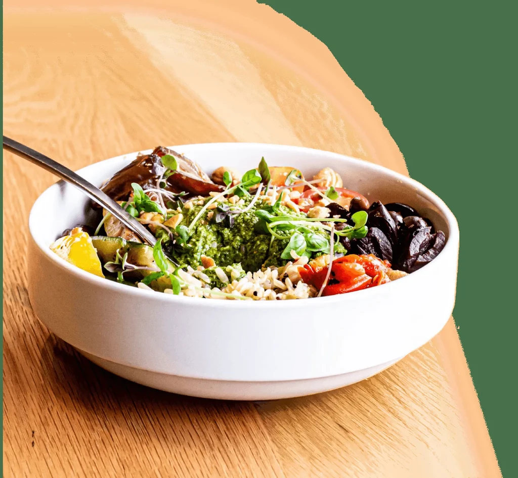 Vibrant food bowl with rice, pesto, roasted vegetables, sprouts, and spoon.