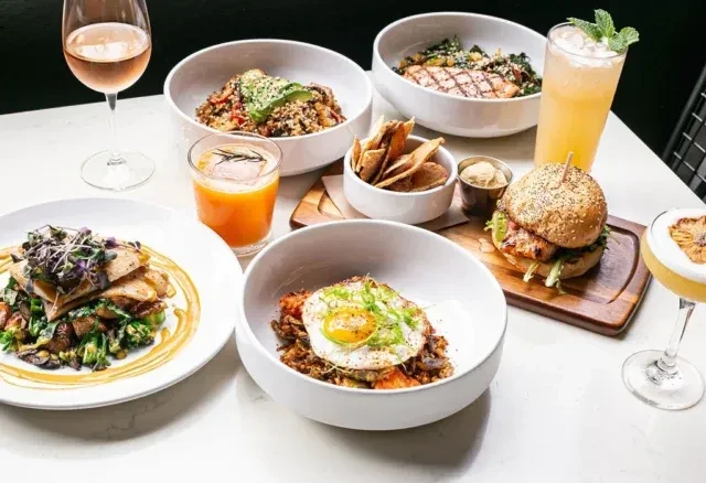 Table featuring a burger, grilled fish, grain bowls, and multiple beverages.