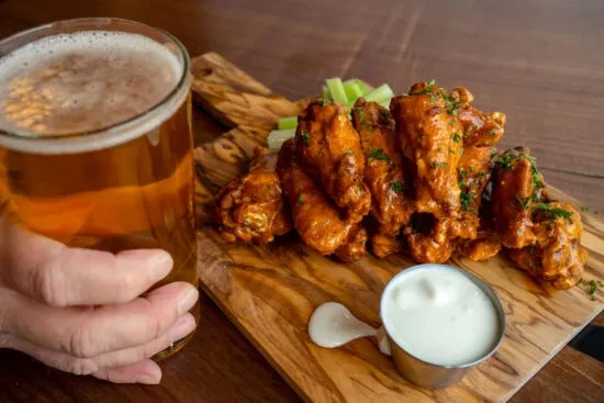 Buffalo wings, celery, sauce, and beer on a rustic wooden board.