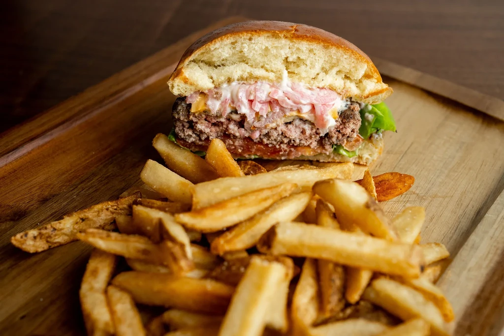 A halved burger showing its layers, alongside golden fries on wood.