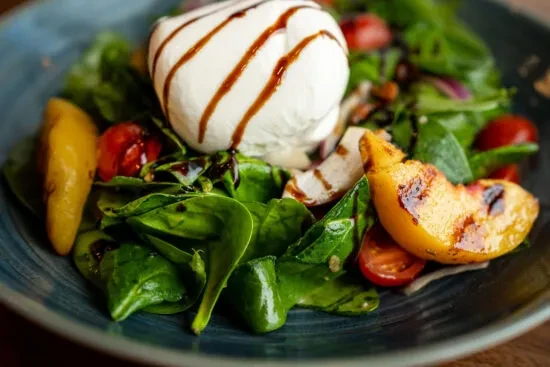 Close-up: Burrata salad with grilled peaches, tomatoes, and greens.