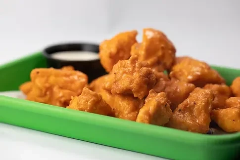 Golden boneless wings in a green tray with white dipping sauce.