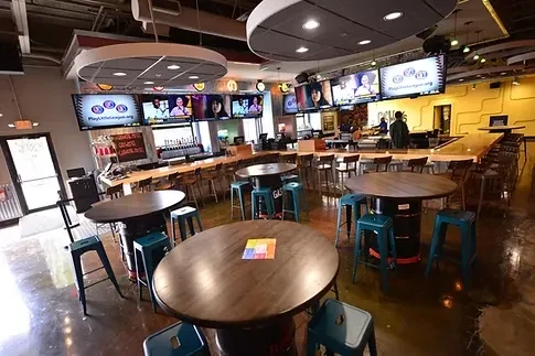 Modern sports bar interior with wooden tables, L-shaped bar, and mounted TVs.