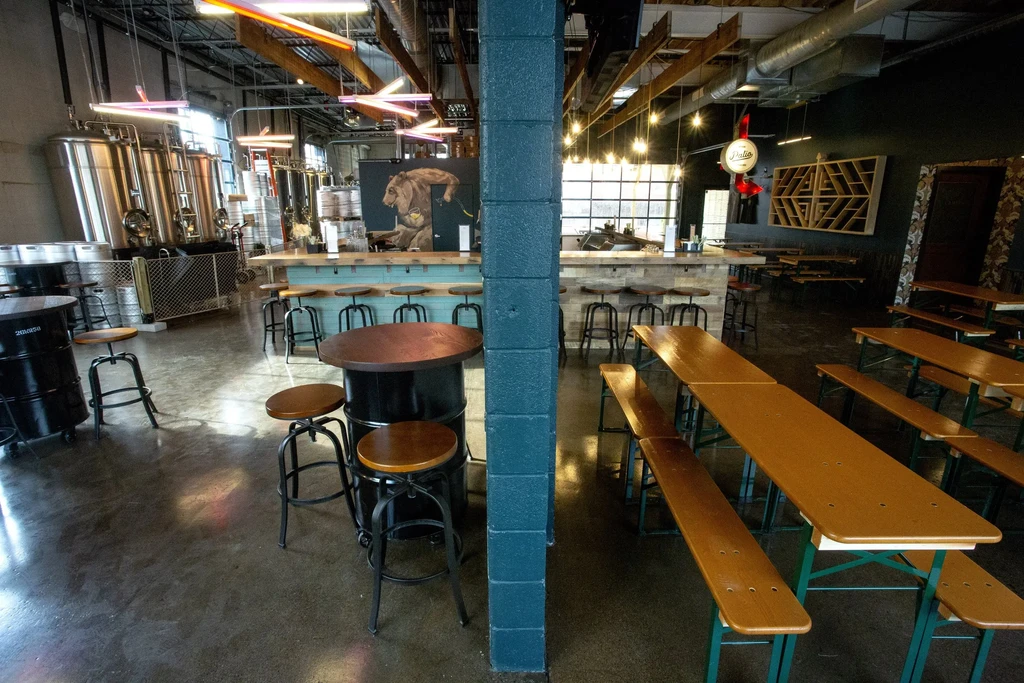 Modern brewery taproom, empty, with steel tanks, bar, and diverse seating.