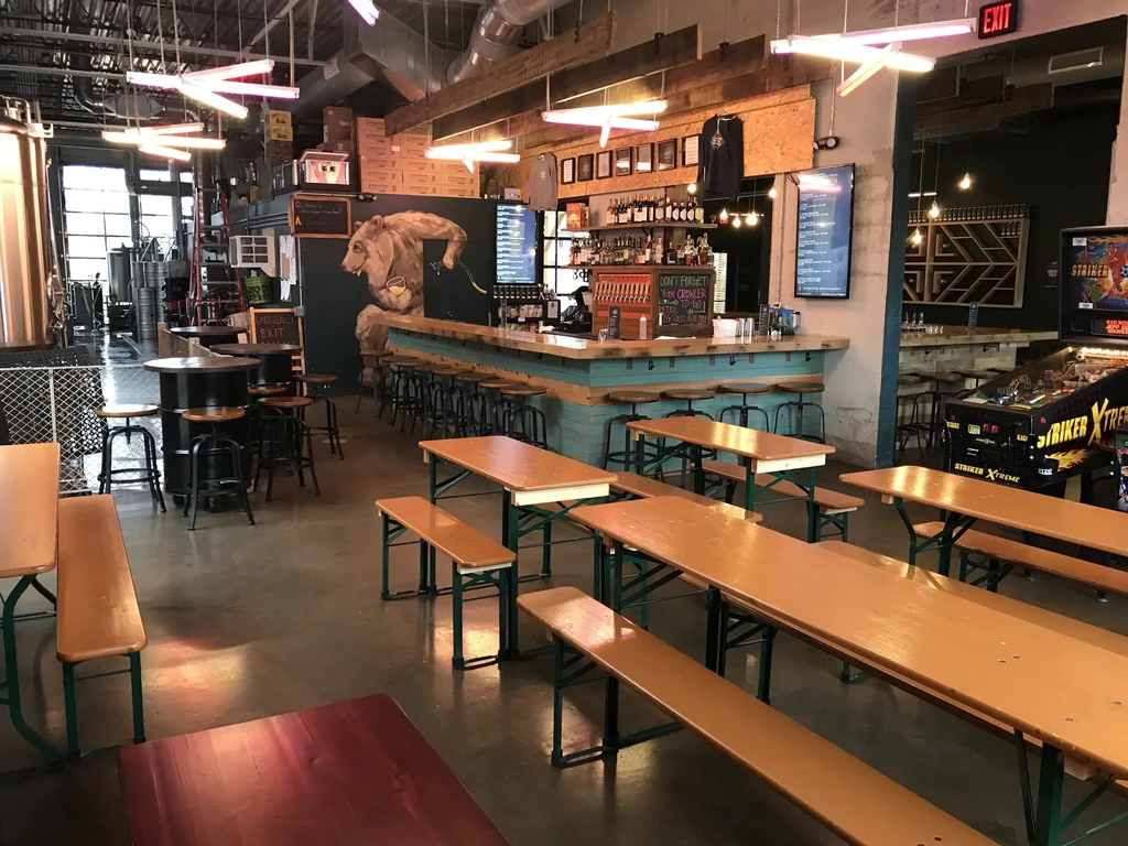 Industrial brewpub interior with teal bar, brewing vats, and bear mural.
