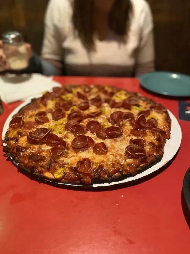 Large pepperoni and banana pepper pizza on a white plate, red table.