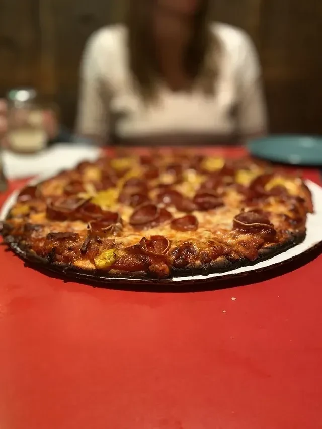 Pepperoni and cheese pizza with yellow toppings on a red table.