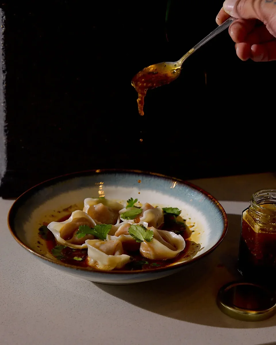 Bowl of dumplings in chili oil with cilantro, spoon above