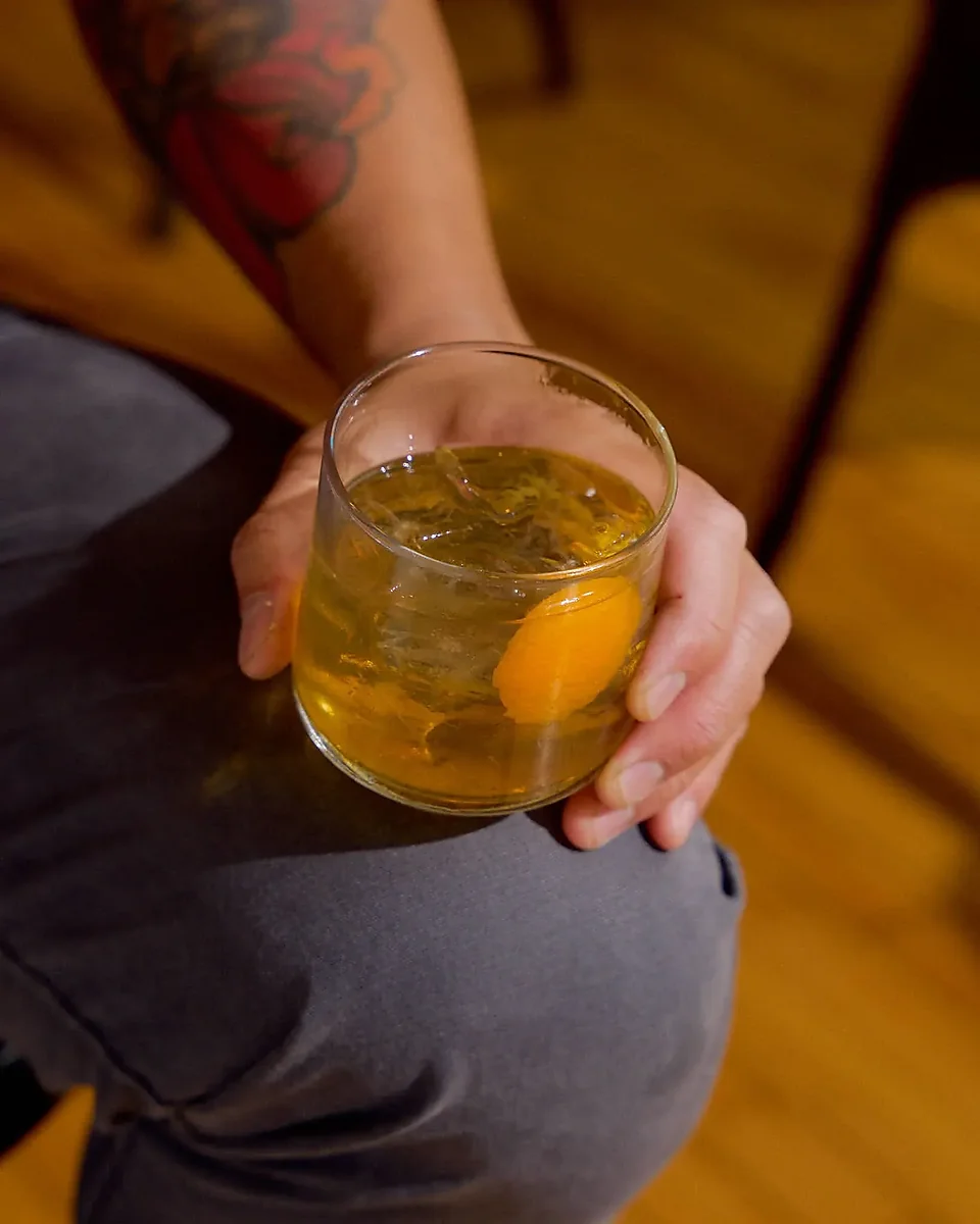 Hand holding an amber cocktail on ice with citrus peel