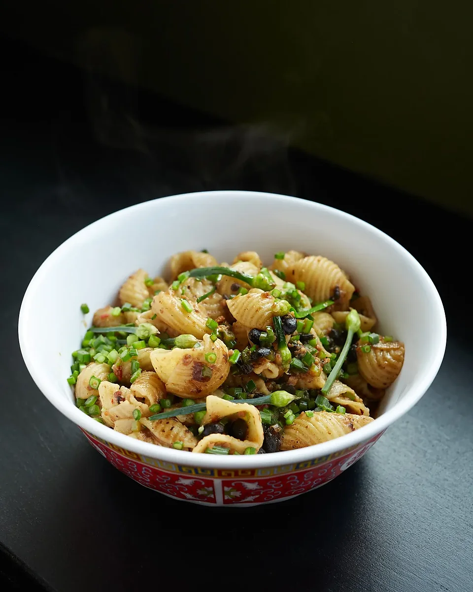 Bowl of shell pasta with scallions and black beans, steaming