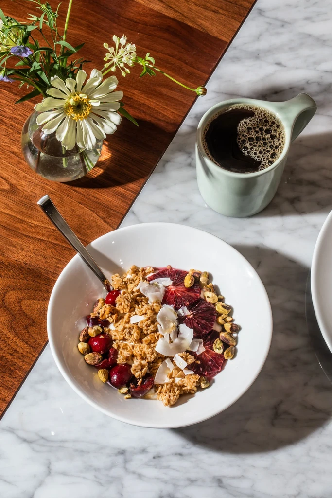Granola parfait, coffee, and zinnia on a wood and marble table.