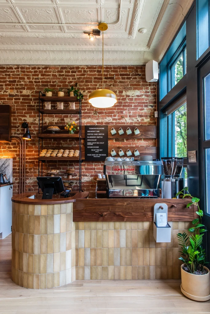 Coffee shop counter with espresso machine, baked goods, and brick wall.