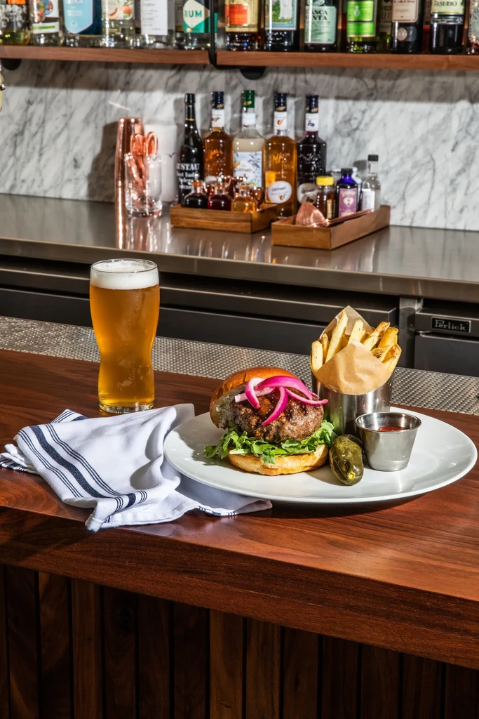 Gourmet burger, fries, beer, and jalapeño on a dark bar counter.