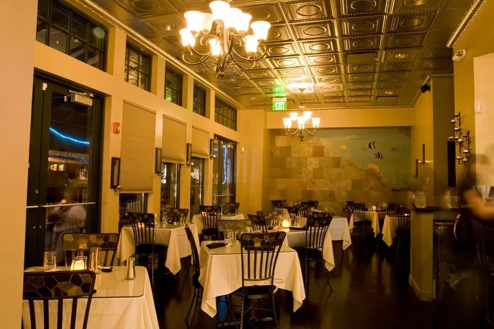 Upscale restaurant dining room with candlelit tables, ornate ceiling, fish mural.
