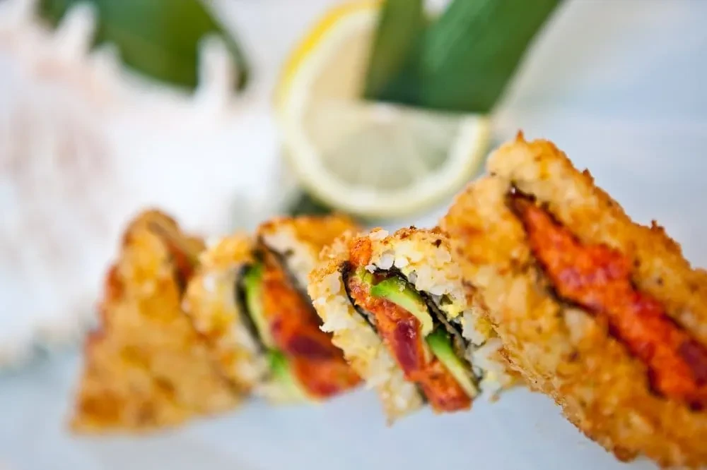 Golden-brown sushi rolls with avocado and reddish filling, garnished with lemon.