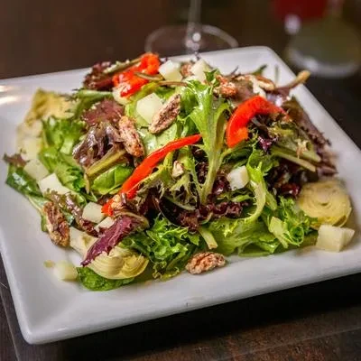Mixed green salad with bell pepper, pecans, white cubes, artichokes.